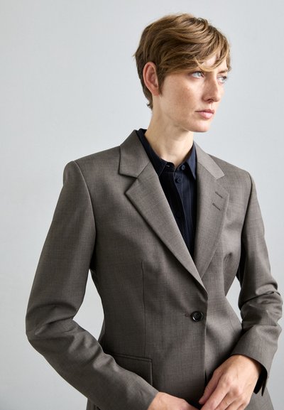 Grauer Blazer mit strukturiertem Design, Ein-Knopf-Verschluss und Reverskragen. Glattes Material und taillierte Passform, kombiniert mit einem dunklen Hemd.