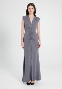 Graues Abendkleid mit tiefem V-Ausschnitt, kurzen Ärmeln und gerafftem Vorderteil. Weicher, schimmernder Stoff mit einem fließenden Rock, kombiniert mit schwarzen Absätzen.
