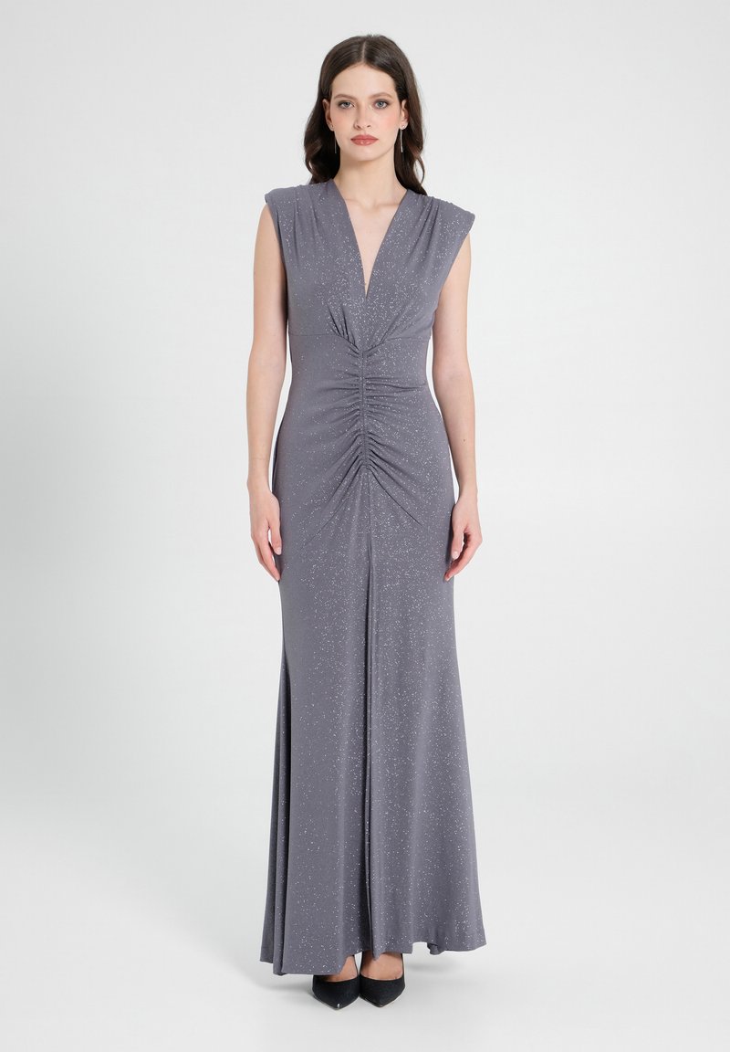 Graues Abendkleid mit tiefem V-Ausschnitt, kurzen Ärmeln und gerafftem Vorderteil. Weicher, schimmernder Stoff mit einem fließenden Rock, kombiniert mit schwarzen Absätzen.