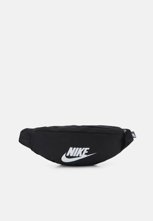 Czarna nerka Nike z białym logo Swoosh na środku z przodu i zamkiem błyskawicznym u góry na jednolitym jasnym tle.