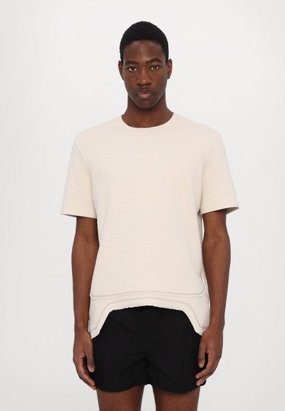 Lichtbeige gestructureerde shirt met korte mouwen en een ronde halslijn, met een licht gebogen zoom en gecombineerd met zwarte shorts.