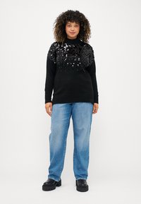 Juodas megztinis su blizgučių tekstūra ant krūtinės, derinamas su šviesiai mėlynomis džinsomis ir juodomis platforminėmis batomis. Paprastas, laisvas kirpimas.