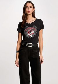 T-shirt nera in cotone con una grafica "Rock & Roll" caratterizzata da un design con rosa e ali. Abbinato a pantaloni neri a vita alta e una cintura larga.