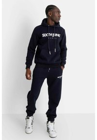 Navyblå hoodie och joggers i bomullsblandning. Innehåller en framficka, dragsko och vitt "SIXTH JUNE"-logotyp. Matchas med vita sneakers.