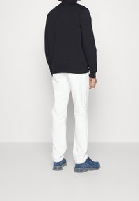 Svart sweatshirt med hög krage, kombinerad med vita byxor och blå skor med texturerad yta och tjocka sulor.