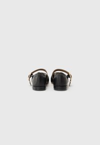Black leather flats with a rounded toe, featuring a brown ankle strap and gold hardware. Smooth texture and minimalist design.
