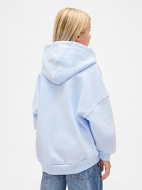 Light blue oversized hoodie with a large hood, ribbed cuffs, and hem. Soft texture with a smooth finish, worn over blue jeans.