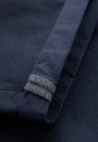 Gros plan sur un tissu bleu foncé avec un poignet replié présentant des coutures détaillées et une doublure intérieure grise texturée.