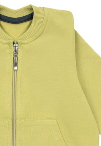 Jasnozielona bluza na zamek z prążkowanym, okrągłym dekoltem, krótkimi rękawami i dwoma przednimi kieszeniami. Gładka faktura z detalem w postaci srebrnego zamka.