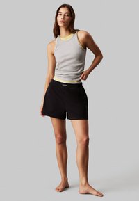 Canottiera grigia a costine con dettagli gialli, abbinata a pantaloni corti neri con vita elastica e logo Calvin Klein.
