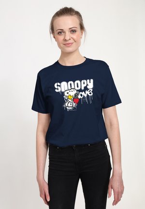 Femme portant un t-shirt bleu marine avec Snoopy tenant un cœur rouge et le texte "Snoopy love" sur fond blanc.