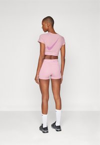 Rosa Nike crop top med korte ermer og en lilla swoosh-logo på baksiden, kombinert med matchende rosa shorts og svarte sko.