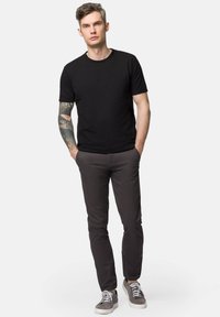 Czarny bawełniany t-shirt z krótkim rękawem, w zestawie z ciemnoszarymi spodniami i szarymi trampkami, z tatuażem na lewym ramieniu.