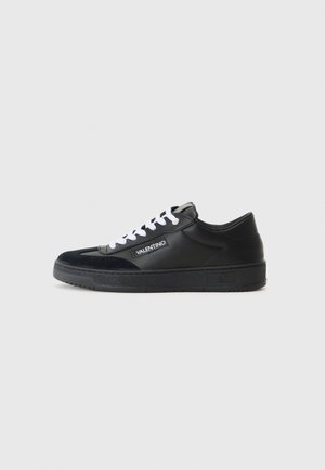 Black leather sneakers with suede accents, white laces, and a branded label on the side. Thick rubber sole with textured grip.