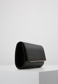 Clutch de cuero negro con un diseño elegante, que presenta una textura suave, un cierre de solapa y un sutil detalle dorado en la parte frontal.