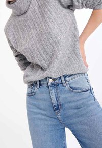 Szary prążkowany sweter z wysokim kołnierzem w zestawieniu z jasnoniebieskimi, wysokim stanem jeansami o minimalistycznych przeszyciach i klasycznym fasonie z pięcioma kieszeniami.