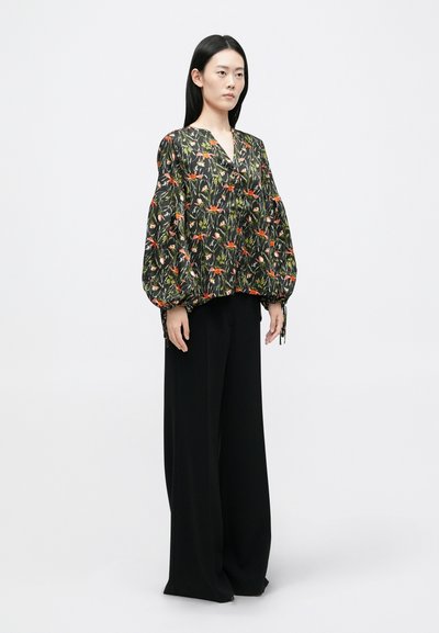 Juostelėta blusa su ilgomis pūkuotomis rankovėmis juodos spalvos, su oranžinėmis, rožinėmis ir žaliomis raštais; derinama su laisvais juodais kelnėmis.