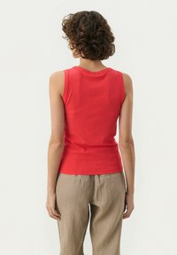 Rød ribbet tanktop med rund halsudsk�æring og skulderstropper, parret med neutralfarvede bukser. Enkel design, tæt pasform.