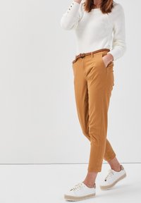 Pull blanc léger et texturé associé à un chino sur mesure jaune moutarde, complété par une ceinture tressée et des espadrilles blanches.