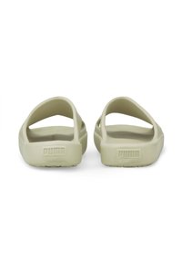 Puma sandaler i lys beige, med en åben bagdesign, blødt gummimateriale og et fremtrædende logo på hælen. Flad, struktureret sål.