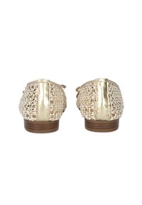 Zapatos tejidos beige con acentos metálicos dorados y un bajo tacón marrón, que presentan un diseño de punto abierto y un respaldo estructurado para mayor soporte.