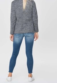 Blazer gris texturizado combinado con jeans ajustados azules. Los jeans presentan un diseño clásico de cinco bolsillos y un lavado desvanecido. Usados con zapatillas blancas.