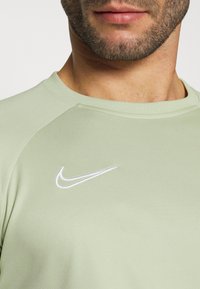 Primer plano de la parte inferior de la cara y el cuello de un hombre que lleva una camiseta Nike de color verde claro con el logo de Nike, en color blanco, en el pecho.