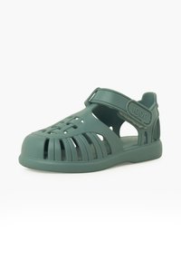 Sandal in plastica verde con design aperto, dotato di fessure orizzontali e verticali per la traspirabilità, cinturino regolabile e soletta texturizzata.