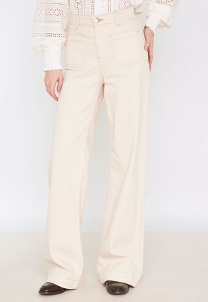 Beige wijde broek met hoge taille, vijf zakken en contrasterende stiksels. De stof lijkt glad met een gestructureerd ontwerp.