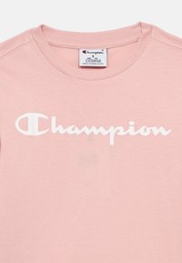 Ανοιχτό ροζ βαμβακερό T-shirt με στρογγυλή λαιμόκοψη, με λευκό λογότυπο «Champion» σε καλλιγραφικό στυλ στο στήθος.