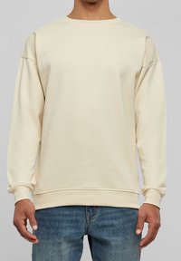 Felpa beige con scollo rotondo e spalle scese. Realizzata in tessuto morbido, presenta polsini e orlo a costine per una vestibilità comoda.