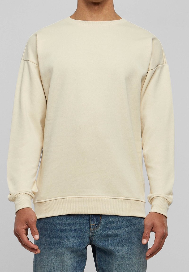 Felpa beige con scollo rotondo e spalle scese. Realizzata in tessuto morbido, presenta polsini e orlo a costine per una vestibilità comoda.