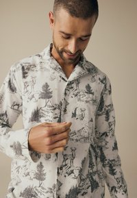 Hemden aus leichtem Stoff mit einem monochromen Druck von Bergen und Wildtieren, detailliert mit Motiven von Bäumen und Rehen, sowie braunen Knöpfen.
