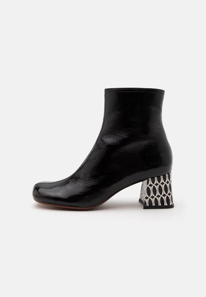 Bottine en cuir verni noir avec un bout carré et un talon épais à motif géométrique noir et blanc.