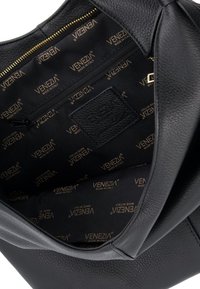 Wnętrze czarnej skórzanej torebki z logo "VENEZIA" w złotym druku, wyposażone w kieszeń na zamek i fakturowaną tkaninę. Gładki, usztywniony design.