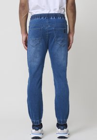 Joggers de denim azul con cintura elástica, tobillos ajustados y dos bolsillos traseros. Textura suave con un ligero desgastado.