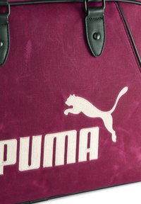 Torba sportowa Puma w ciemnoróżowym materiale z czarnymi skórzanymi akcentami, z białym haftowanym logo i sylwetką skaczącego kota.