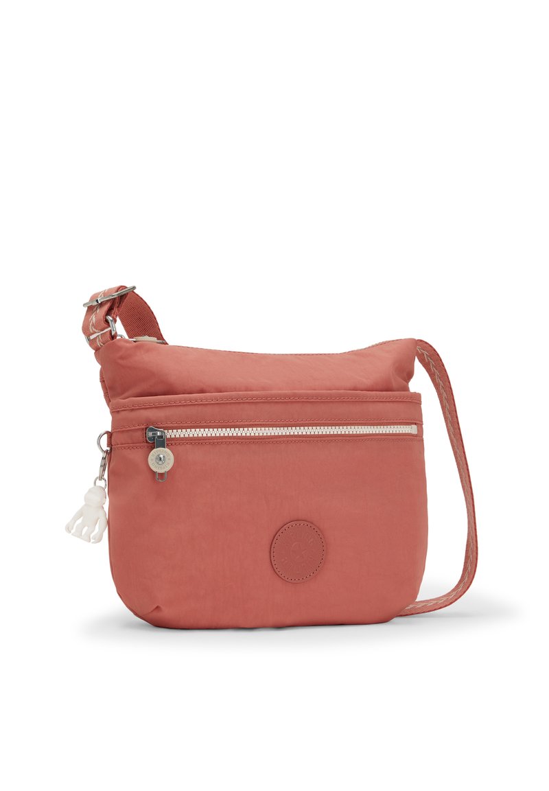 Bolso cruzado de tela coral con un bolsillo delantero con cremallera, logo circular y correa ajustable. Textura suave con un diseño sencillo.