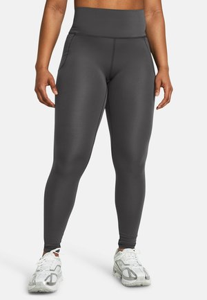 Leggings taille haute gris foncé en tissu extensible, dotés de poches latérales et d'une texture lisse, associés à des chaussures de sport blanches.