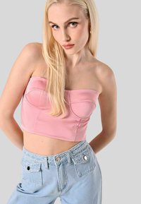 Top corto strapless rosa con cuciture curve, abbinato a jeans di denim azzurri a vita alta con cintura testurizzata e tasche frontali.