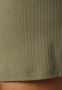Shorts en tissu côtelé vert olive avec une coupe près du corps. Présente une texture lisse et des coutures soignées au niveau de l'ourlet.