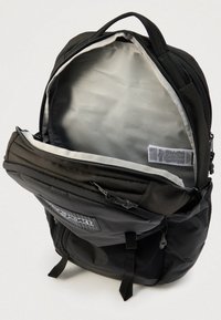 Μαύρο σακίδιο πλάτης με το κύριο διαμέρισμα ανοιχτό, που δείχνει το εσωτερικό φόδρα σε ανοιχτό γκρι και την ετικέτα φροντίδας υφάσματος στο εσωτερικό.