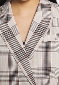 Blazer a righe con un motivo geometrico in tonalità beige, nero e marrone, dotato di revers e tessuto testurizzato.