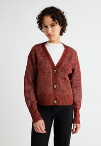 Rust-colored ribbed cardigan with a V-neck, three large buttons, and long sleeves, made from textured knit material.