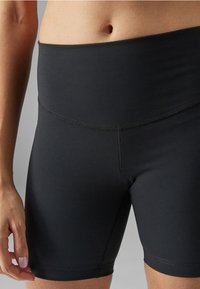 Højtaljede sorte korte træningsshorts lavet af strækbart materiale, med flade sømme og en tætsiddende design for komfort og fleksibilitet.