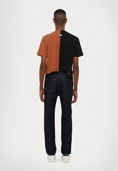 Cropped t-shirt with a color-block design; left side brown, right side black. Paired with dark denim jeans and white sneakers.