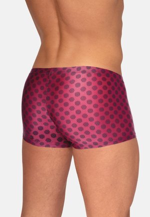 Mannelijk bovenlichaam en bovenbenen gekleed in nauwsluitende paarse korte broek met een zwart cirkelvormig stippenpatroon, gezien van achteren.