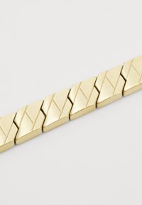 Bracelet en métal doré avec une série de maillons en forme de losange, présentant une texture brossée et des motifs angulaires gravés.