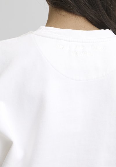 Sudadera blanca con cuello acanalado y tejido texturizado. La parte trasera presenta un texto en relieve que dice "TODOS LOS JEANS ORIGINAL."