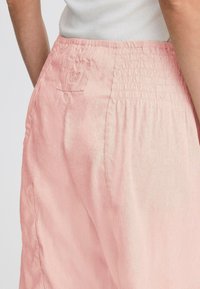 Pantalons en lin rose pâle avec une taille élastique, dotés d'une petite poche arrière et d'une coupe décontractée. Texture douce avec peu de plis.